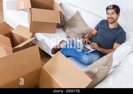 Asian Chinese Korean man packing or unpacking boxes using a laptop computer on the internet and moving into a new home. Stock Photo