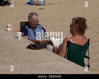 middle aged couple sat at the beach reading, Lyme Regis, Dorset, UK Stock Photo