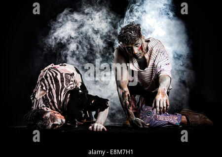 Two male zombies crawling on their knees, on black smoky background, looking at camera. Halloween theme Stock Photo