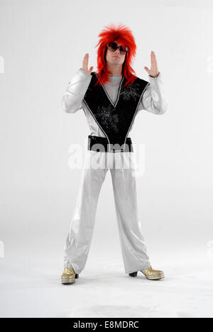 man in fancy dress, comedy costume as a ziggy stardust david bowie, space age character, with shiny silver suit, wig & platforms Stock Photo