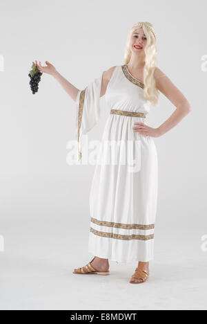 girl dressed in fancy dress comedy costume as a roman / edyptian lady in a white skirt, blond wig, sandals and grapes Stock Photo