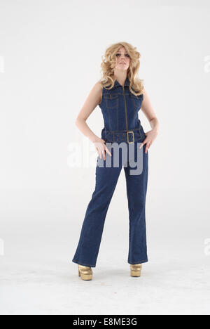 Woman in fancy dress comedy costume in a 1970s, demin disco catsuit outfit, with gold platform shoes, wig in 70s style hair Stock Photo