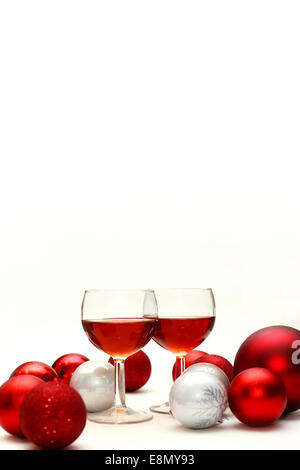 Two wine glasses filled with red wine sit on an isolated white background in surrounded by silver and red sparkling Christmas Bu Stock Photo