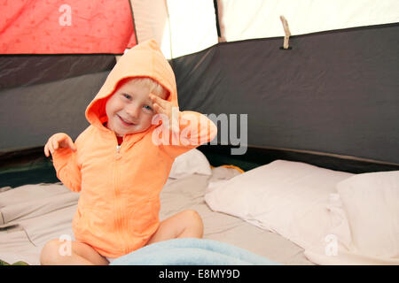 A happy young boy child is waking up in a tent after spending the night camping. Stock Photo