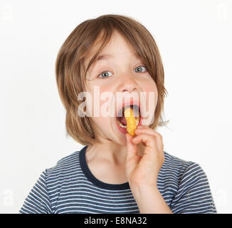 A boy with brown long hair shoves peanut flips in the mouth Stock Photo