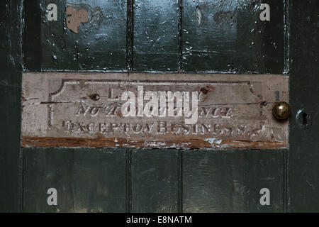 A worn sign with a message which reads 'Laundry No Admittance Except on Business' on a old wooden door with green, peeling paint Stock Photo