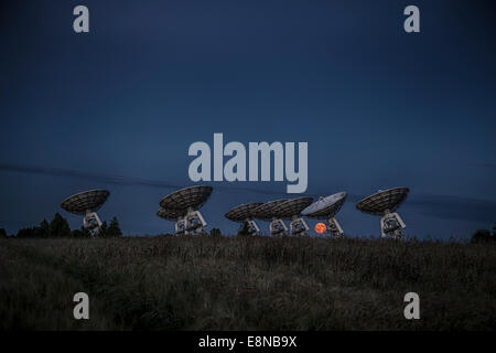 The full moon rises over the horizon behind a radio telescope array as the sun sets Stock Photo