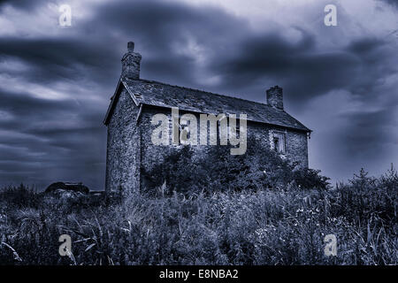 Spooky, haunted, derelict house with broken windows under a stormy sky. Black and white with a blue tint effect. Stock Photo