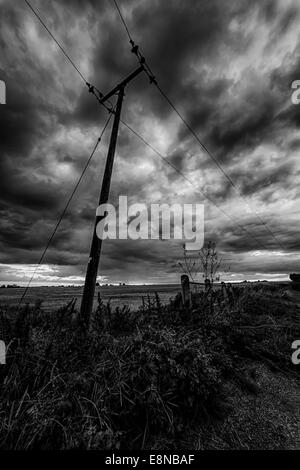 Silhouette of a telegraph pole at dusk with angry dark clouds in the sky in black and white Stock Photo