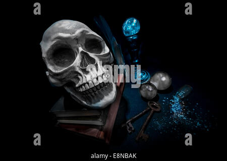 Human skull on book in a pool of light. Crystal balls glowing and cloudy. Spilled glass jar and two rusty old keys. Weird wide a Stock Photo