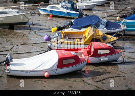 Small colourful glass fibre boats at rest on their moorings lie on the sand at low tide in a harbour. Stock Photo