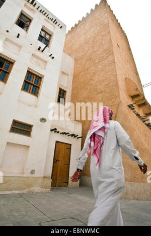 A Qatari man walking past traditional houses in the street in Doha Qatar Stock Photo