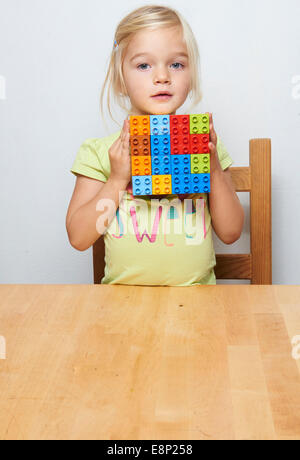 Portrait of Little child blond girl playing with plastic building blocks, white background Stock Photo