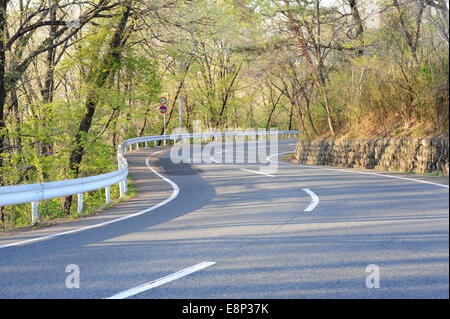 An empty winding mountain road lined with trees and a raised shoulder in the early evening in Takasaki, Gunma Prefecture, Japan. Stock Photo