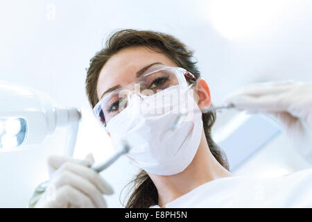 Dentist wearing surgical mask while holding angled mirror and drill, ready to begin Stock Photo