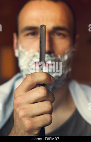 Young man getting an old-fashioned shave with straight razor. Closeup, retro styled imagery Stock Photo