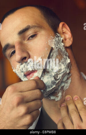 Young man getting an old-fashioned shave with straight razor. Closeup, retro styled imagery Stock Photo