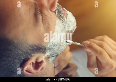 Young man getting an old-fashioned shave with straight razor. Closeup, retro styled imagery Stock Photo