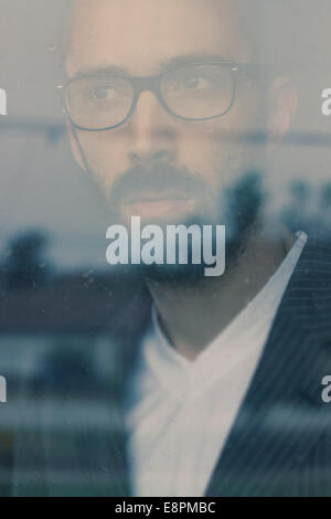 Portrait of a handsome man with beard, wearing suit and glasses. Daydreaming and looking through the window Stock Photo
