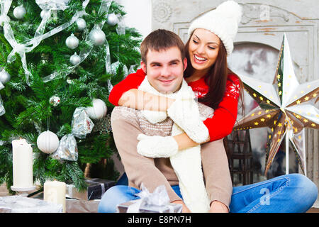 Young happy smiling couple sitting by Christmas tree Stock Photo