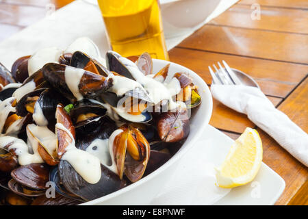 Plate full of mussels with garlic sauce on wooden table in restaurant Stock Photo