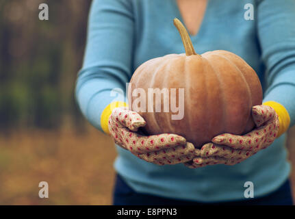 Woman wearing gloves holding big orange pumpkin in her hands Stock Photo