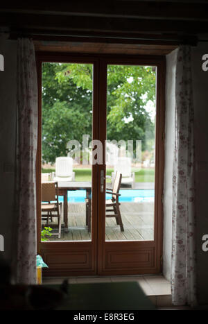 Looking through the French Doors of a French holiday cottage into the garden with a patio and pool Stock Photo