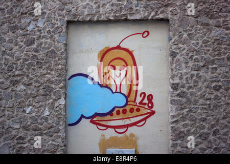 A painting of an alien smiling driving an UFO behind a blue cloud decorates a wall in Granada, Andalusia, Spain Stock Photo