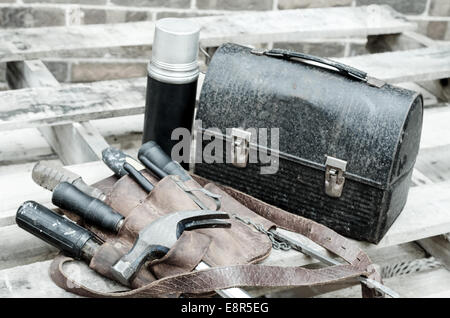 Construction worker's lunch break with lunch pail, beverage container, tool belt, hammer, screwdrivers, and wrenches on wooden p Stock Photo