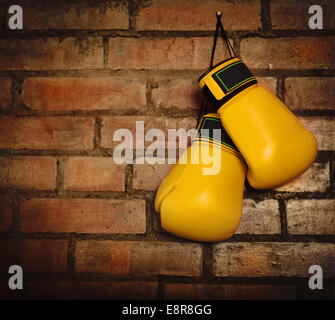 Pair of yellow boxing gloves hanging on a brick wall Stock Photo