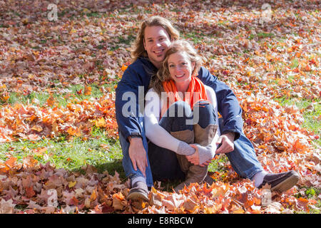 Young couple sitting inside a heart made of fallen autumn colourful leaves Stock Photo
