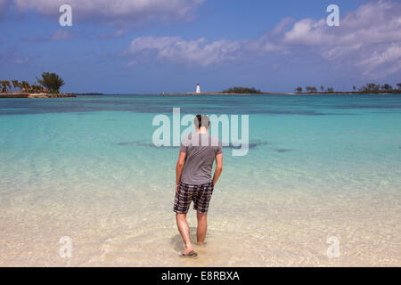 Young man in shorts and a grey shirt seen from behind as he walks into the Caribbean Sea at Nassau, Bahamas. Stock Photo