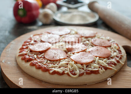 Freshly prepared pepperoni pizza with rolling pin and fresh ingredients Stock Photo