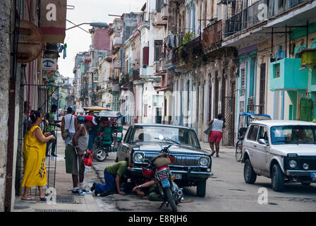 Havana Cuba - Onlookers watch as two men attempt to do improvised repairs on a vintage American car in a Central Havana street. Stock Photo