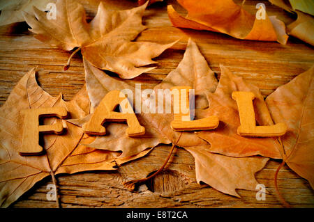 wooden letters forming the word fall and some autumn leaves on a weathered wooden background Stock Photo