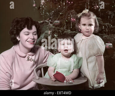 1950s PORTRAIT SMILING MOTHER TWO CHILDREN GIRLS BY CHRISTMAS TREE Stock Photo