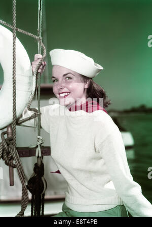 1940s PORTRAIT SMILING WOMAN WEARING SAILOR HAT YACHTING OUTFIT POSING BY SAILBOAT RIGGING LOOKING AT CAMERA Stock Photo
