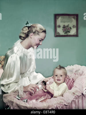 1940s 1950s SMILING WOMAN MOTHER FEEDING BABY BOTTLE IN BASSINET Stock Photo