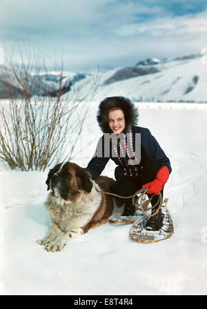 1940s 1950s SMILING WOMAN WEARING SNOWSHOES CROUCHING PETTING ST. BERNARD DOG Stock Photo