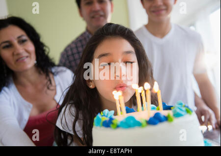 Hispanic girl blowing out candles on birthday cake Stock Photo