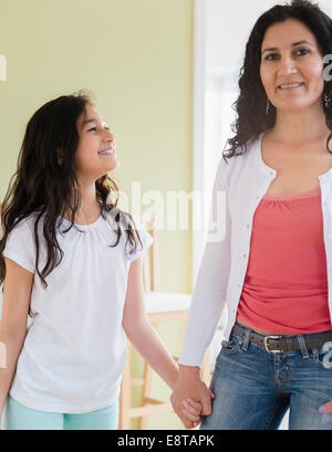 Hispanic mother and daughter holding hands in living room Stock Photo