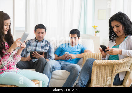 Hispanic family using cell phones and digital tablets in living room