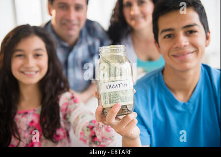 Hispanic family holding full vacation savings jar Stock Photo