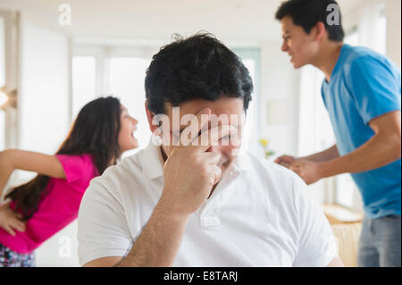 Hispanic father covering his face as children fight behind him Stock Photo