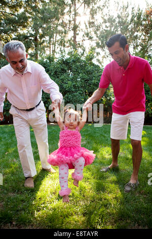 Father and grandfather helping daughter walk in backyard Stock Photo