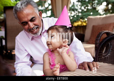 Grandfather sitting with granddaughter at birthday party Stock Photo