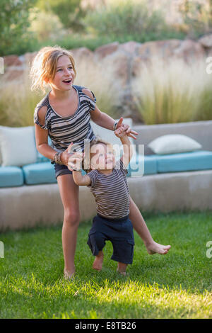 Caucasian sister helping toddler brother walk in backyard Stock Photo