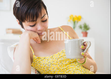 Fatigued mixed race woman drinking cup of coffee