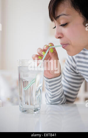 Mixed race woman drinking water with straw Stock Photo