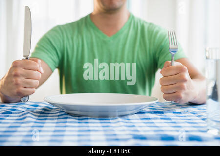 Mixed race man holding fork and knife at table Stock Photo